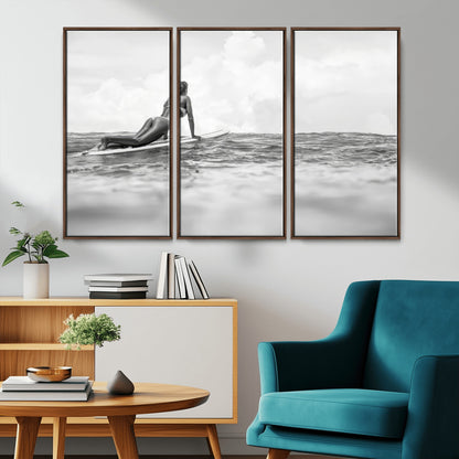 A black and white ocean scene featuring a surfer girl waiting on her board, gazing at the horizon, capturing a tranquil and adventurous coastal moment.