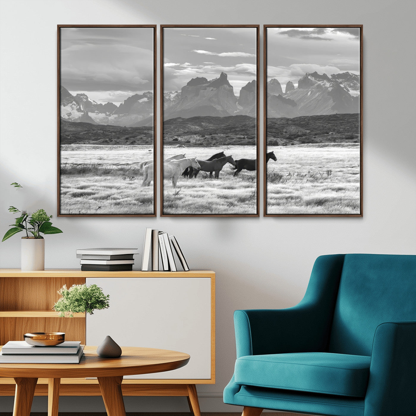 A black and white landscape of wild horses grazing in a vast grassland with towering mountains in the background, creating a moody and rustic western aesthetic.