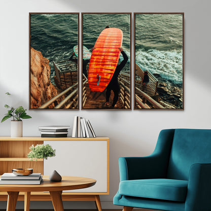 A surfer carrying a bold orange surfboard down a rugged staircase toward the ocean, bathed in golden hour light, capturing the energy of coastal adventure.