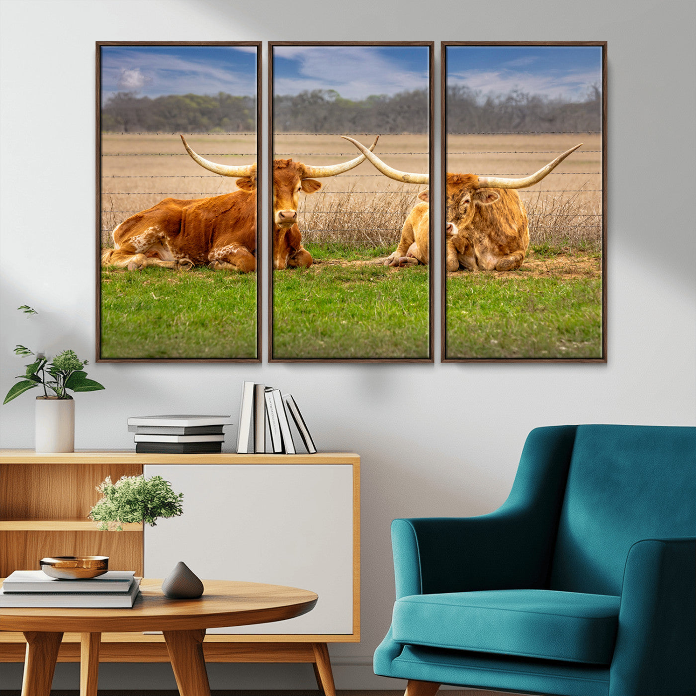 Two longhorn cows lying on green grass in front of a golden field and trees under a blue sky, perfect for rustic country wall decor.