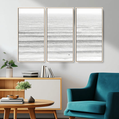 Monochrome photo of a lone surfer in calm layered waves, perfect for minimalist coastal or moody ocean-inspired wall decoration.