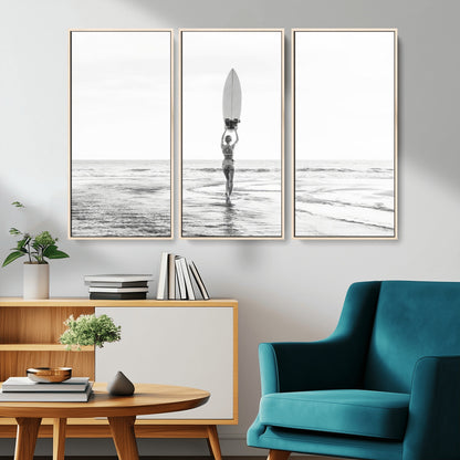 Black and white image of a female surfer holding a surfboard above her head while walking toward the ocean, creating a minimalist and bold coastal aesthetic.