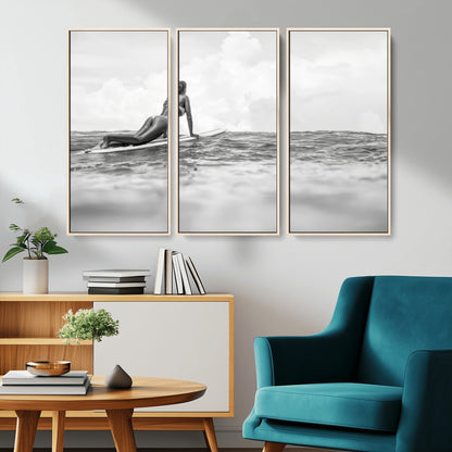 A black and white ocean scene featuring a surfer girl waiting on her board, gazing at the horizon, capturing a tranquil and adventurous coastal moment.