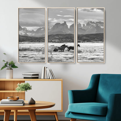 A black and white landscape of wild horses grazing in a vast grassland with towering mountains in the background, creating a moody and rustic western aesthetic.