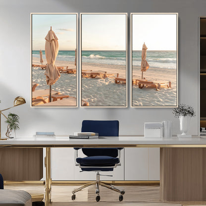 Minimalist photo of empty beach loungers and umbrellas on soft sand, ideal for calm seaside or pastel coastal-style home decor.