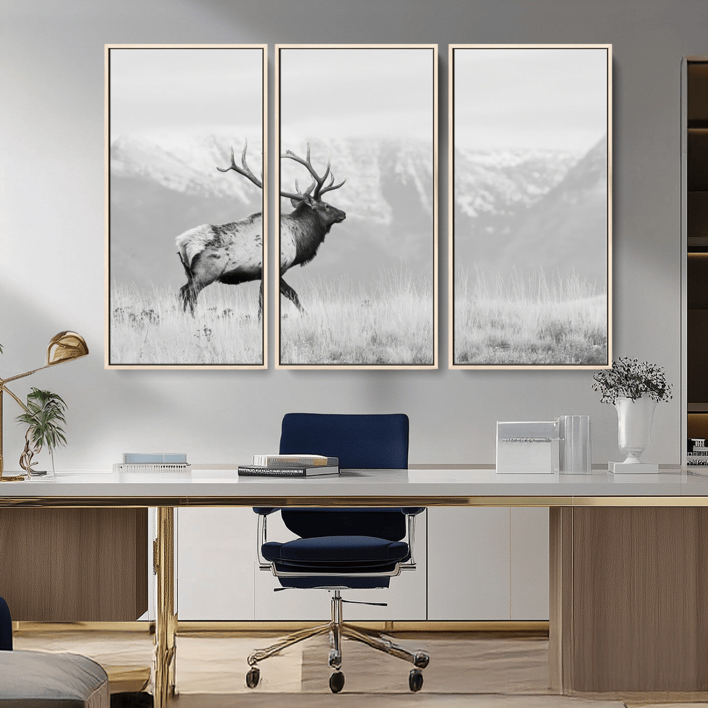 Black and white photograph of a majestic elk standing in a grassy field with snow-capped mountains in the background, creating a bold and rustic wilderness scene.