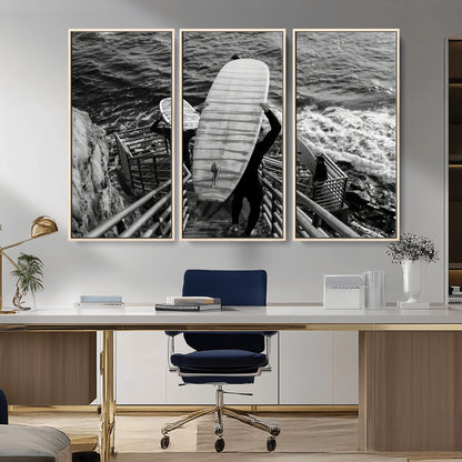 Black and white photo of surfers carrying boards down a rugged cliffside stairway, capturing a bold and adventurous coastal scene.