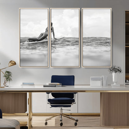 A black and white ocean scene featuring a surfer girl waiting on her board, gazing at the horizon, capturing a tranquil and adventurous coastal moment.