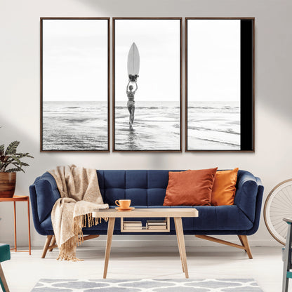 Black and white image of a female surfer holding a surfboard above her head while walking toward the ocean, creating a minimalist and bold coastal aesthetic.