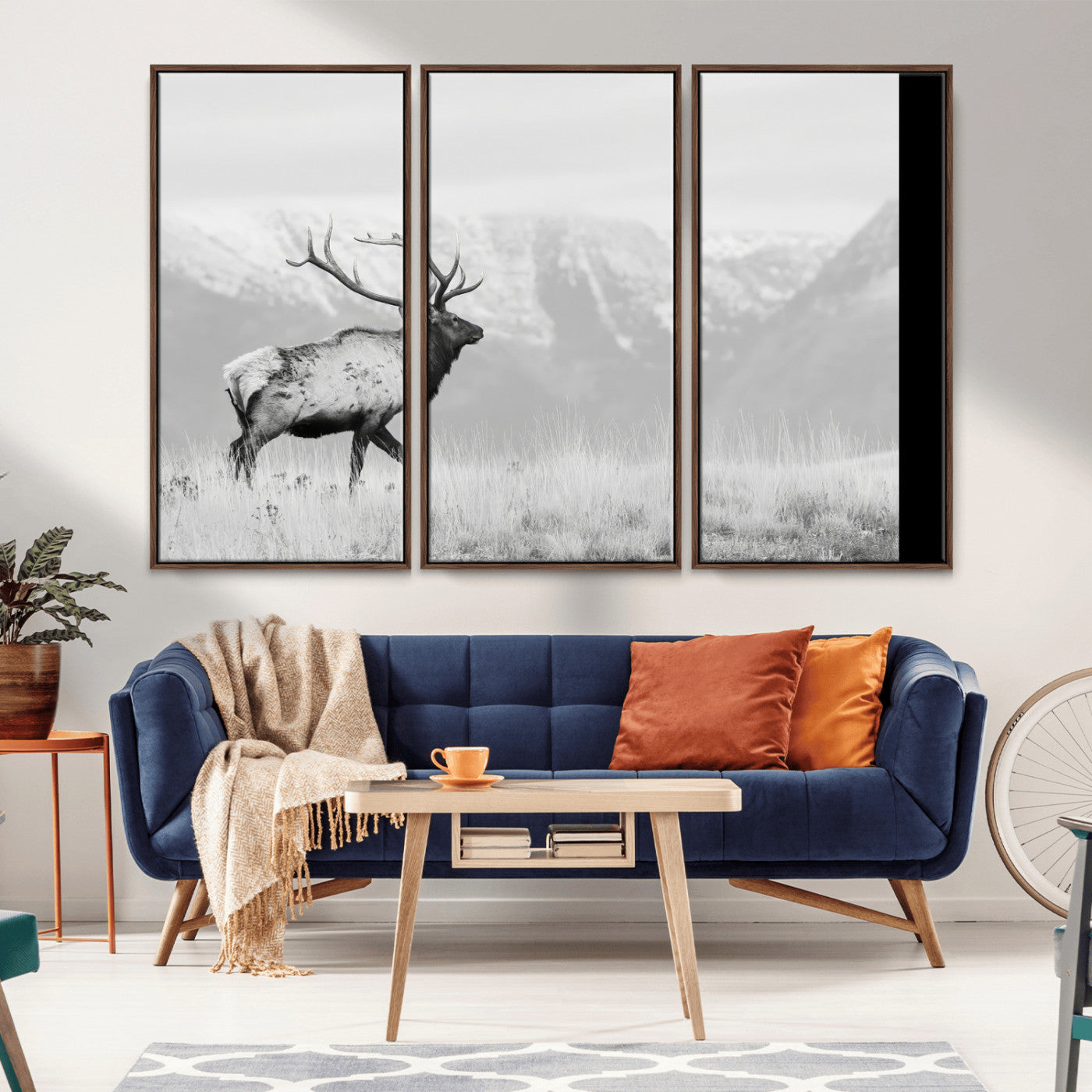 Black and white photograph of a majestic elk standing in a grassy field with snow-capped mountains in the background, creating a bold and rustic wilderness scene.