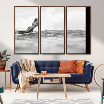 A black and white ocean scene featuring a surfer girl waiting on her board, gazing at the horizon, capturing a tranquil and adventurous coastal moment.