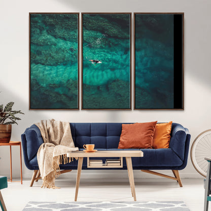 An aerial view of a solo surfer paddling through crystal-clear turquoise waters over a sunlit reef, capturing the beauty and serenity of open water surfing.