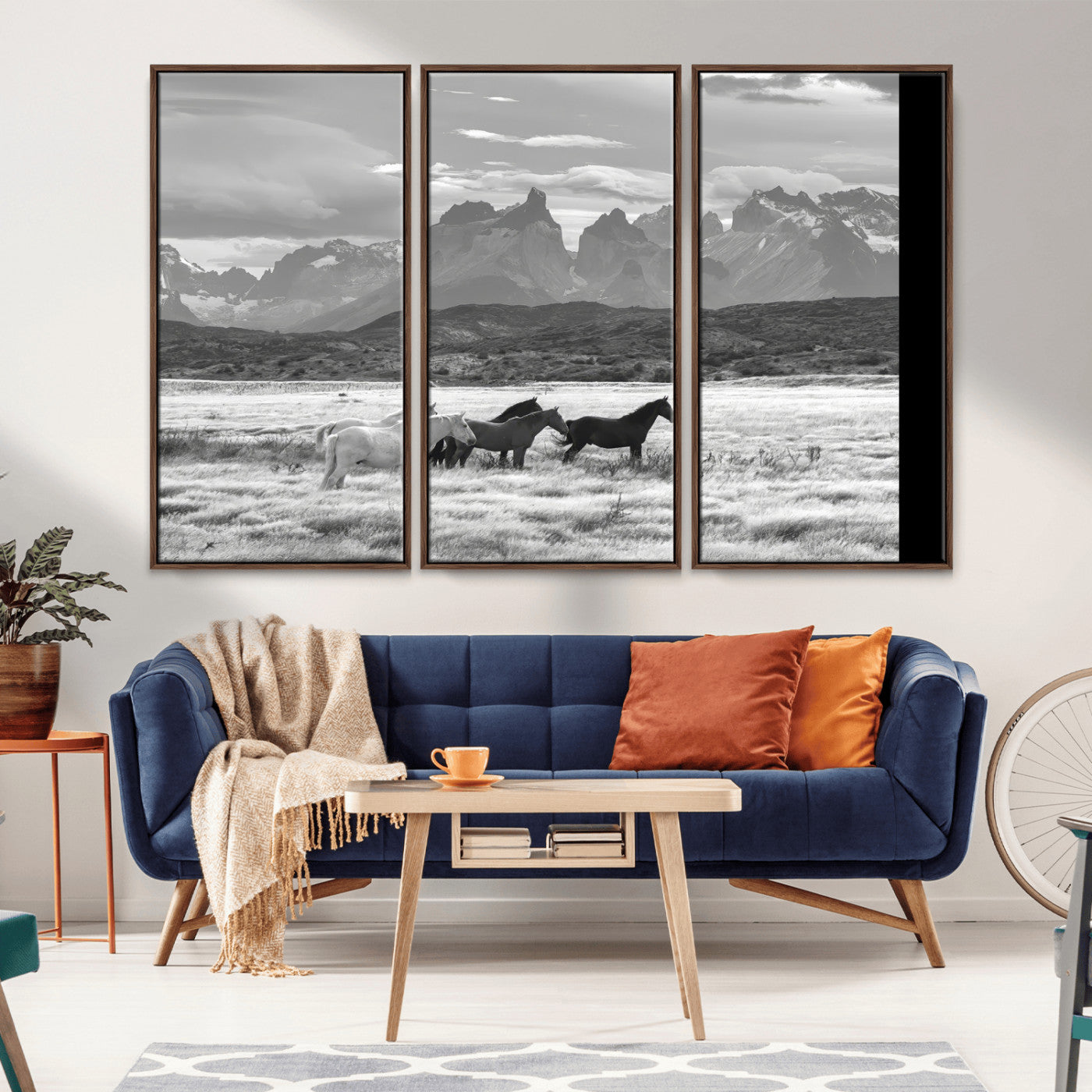A black and white landscape of wild horses grazing in a vast grassland with towering mountains in the background, creating a moody and rustic western aesthetic.