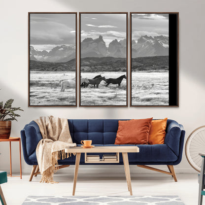 A black and white landscape of wild horses grazing in a vast grassland with towering mountains in the background, creating a moody and rustic western aesthetic.