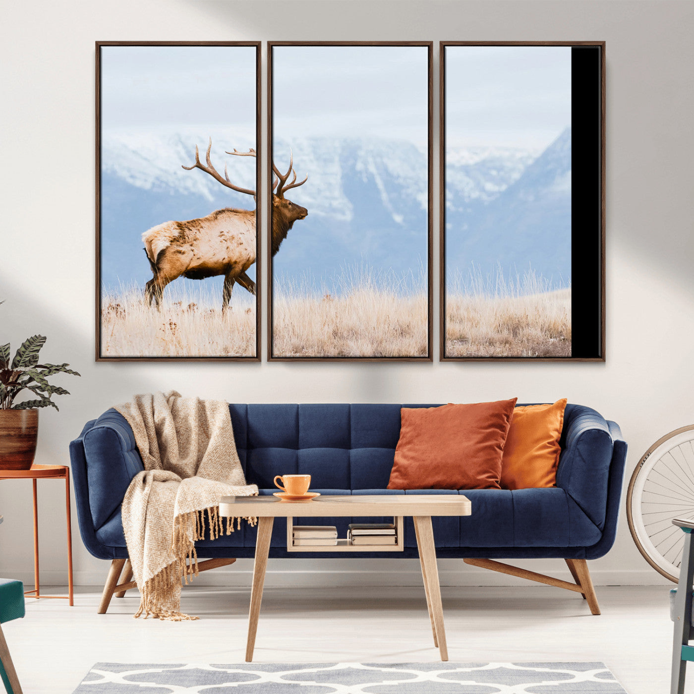 An elk walking on snowy grassland with majestic mountains in the background, ideal for rustic lodge or cabin wall decor.
