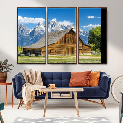 A rustic wooden barn sits in front of towering mountain peaks under a clear blue sky, perfect for farmhouse or cabin style interiors.