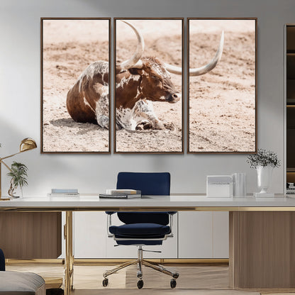 Texas Longhorn bull resting on dusty ground with warm tones, ideal for rustic western or farmhouse-themed wall decor.