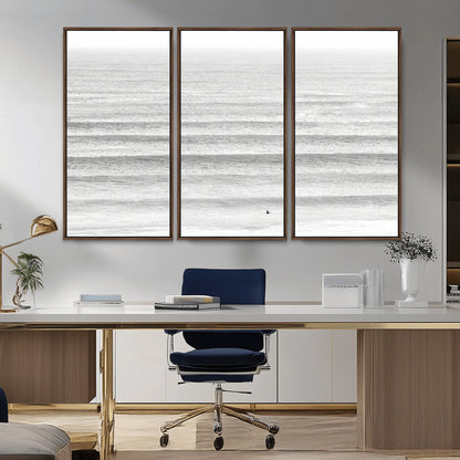 Monochrome photo of a lone surfer in calm layered waves, perfect for minimalist coastal or moody ocean-inspired wall decoration.