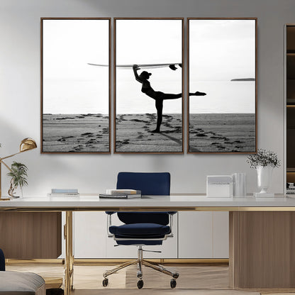 A woman balances a surfboard on her head while striking a yoga pose on the beach, silhouetted against a calm ocean horizon.