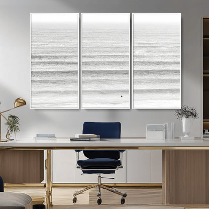 Monochrome photo of a lone surfer in calm layered waves, perfect for minimalist coastal or moody ocean-inspired wall decoration.