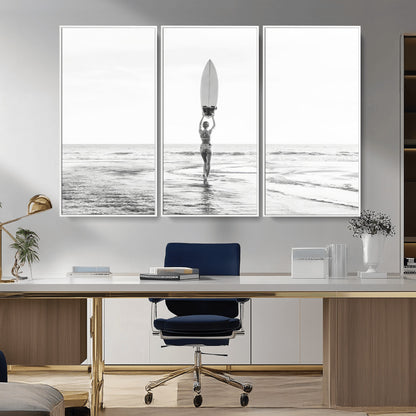 Black and white image of a female surfer holding a surfboard above her head while walking toward the ocean, creating a minimalist and bold coastal aesthetic.