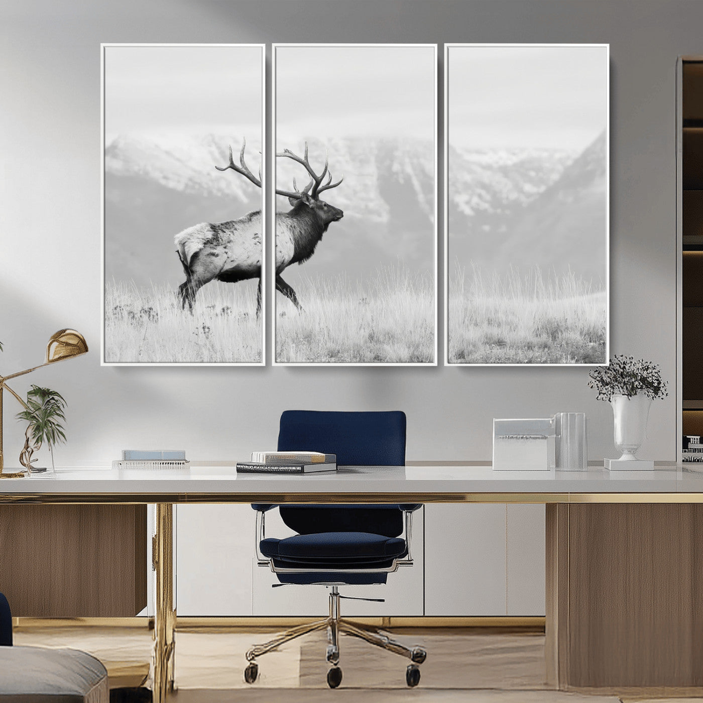 Black and white photograph of a majestic elk standing in a grassy field with snow-capped mountains in the background, creating a bold and rustic wilderness scene.