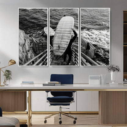 Black and white photo of surfers carrying boards down a rugged cliffside stairway, capturing a bold and adventurous coastal scene.