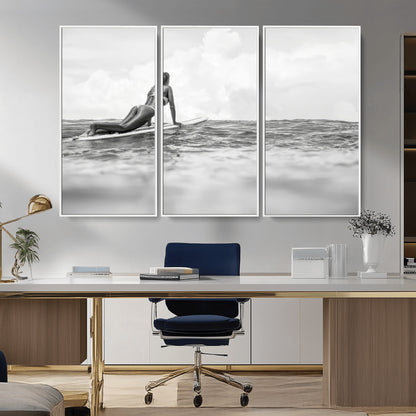 A black and white ocean scene featuring a surfer girl waiting on her board, gazing at the horizon, capturing a tranquil and adventurous coastal moment.