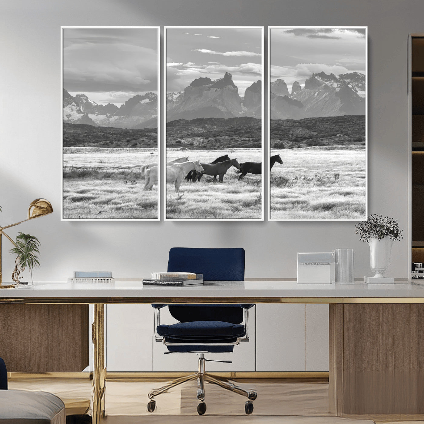 A black and white landscape of wild horses grazing in a vast grassland with towering mountains in the background, creating a moody and rustic western aesthetic.