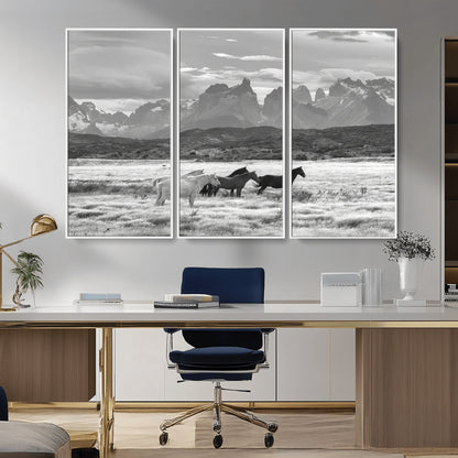 A black and white landscape of wild horses grazing in a vast grassland with towering mountains in the background, creating a moody and rustic western aesthetic.