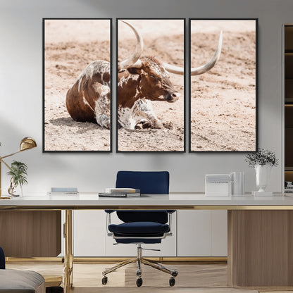 Texas Longhorn bull resting on dusty ground with warm tones, ideal for rustic western or farmhouse-themed wall decor.