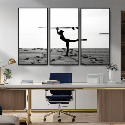 A woman balances a surfboard on her head while striking a yoga pose on the beach, silhouetted against a calm ocean horizon.