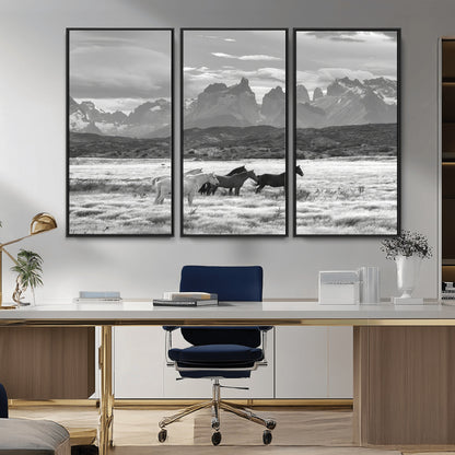 A black and white landscape of wild horses grazing in a vast grassland with towering mountains in the background, creating a moody and rustic western aesthetic.