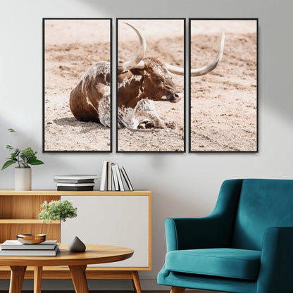 Texas Longhorn bull resting on dusty ground with warm tones, ideal for rustic western or farmhouse-themed wall decor.