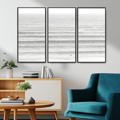 Monochrome photo of a lone surfer in calm layered waves, perfect for minimalist coastal or moody ocean-inspired wall decoration.