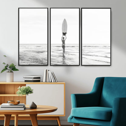 Black and white image of a female surfer holding a surfboard above her head while walking toward the ocean, creating a minimalist and bold coastal aesthetic.