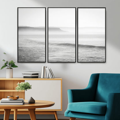 A black and white minimalist seascape featuring soft rolling waves and misty distant cliffs, creating a serene and timeless coastal atmosphere.