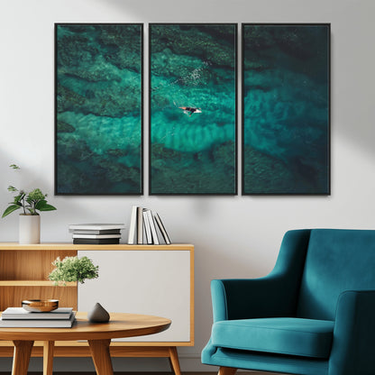 An aerial view of a solo surfer paddling through crystal-clear turquoise waters over a sunlit reef, capturing the beauty and serenity of open water surfing.