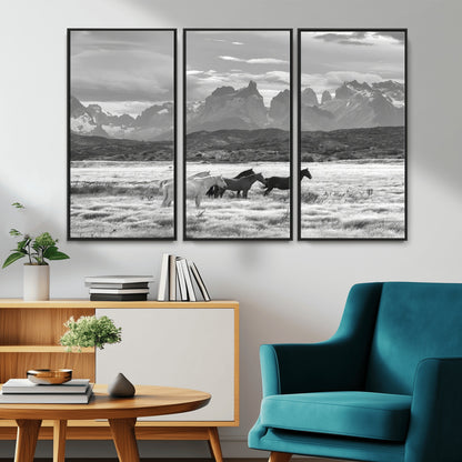A black and white landscape of wild horses grazing in a vast grassland with towering mountains in the background, creating a moody and rustic western aesthetic.