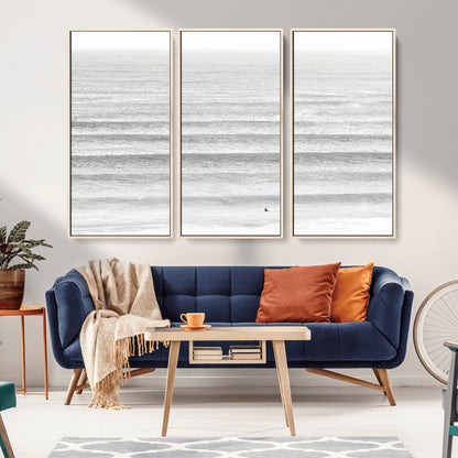 Monochrome photo of a lone surfer in calm layered waves, perfect for minimalist coastal or moody ocean-inspired wall decoration.