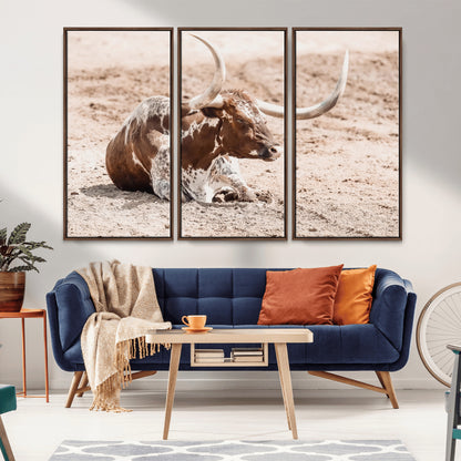 Texas Longhorn bull resting on dusty ground with warm tones, ideal for rustic western or farmhouse-themed wall decor.