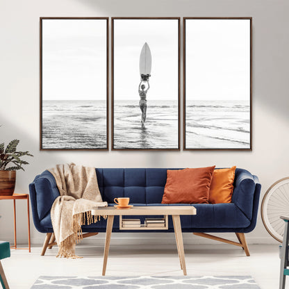Black and white image of a female surfer holding a surfboard above her head while walking toward the ocean, creating a minimalist and bold coastal aesthetic.