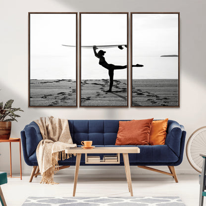 A woman balances a surfboard on her head while striking a yoga pose on the beach, silhouetted against a calm ocean horizon.