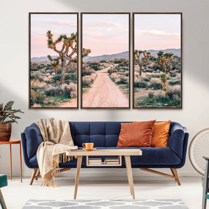 A dusty road winding through Joshua Tree National Park, framed by iconic twisted trees and warm desert tones under a soft pastel sky.