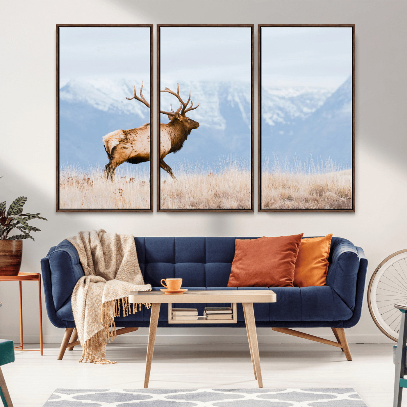 An elk walking on snowy grassland with majestic mountains in the background, ideal for rustic lodge or cabin wall decor.