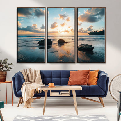 A serene beach at sunset with vibrant clouds, calm water, and rocks in the foreground reflecting the warm colors of the setting sun.