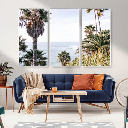Scenic coastal view with tall palm trees overlooking a calm ocean, soft blue waves, and surfers in the distance, creating a peaceful tropical vibe.