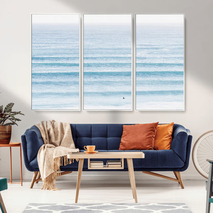 Minimalist ocean view with soft blue waves and a lone surfer, creating a serene and airy coastal aesthetic, perfect for tranquil home decor.