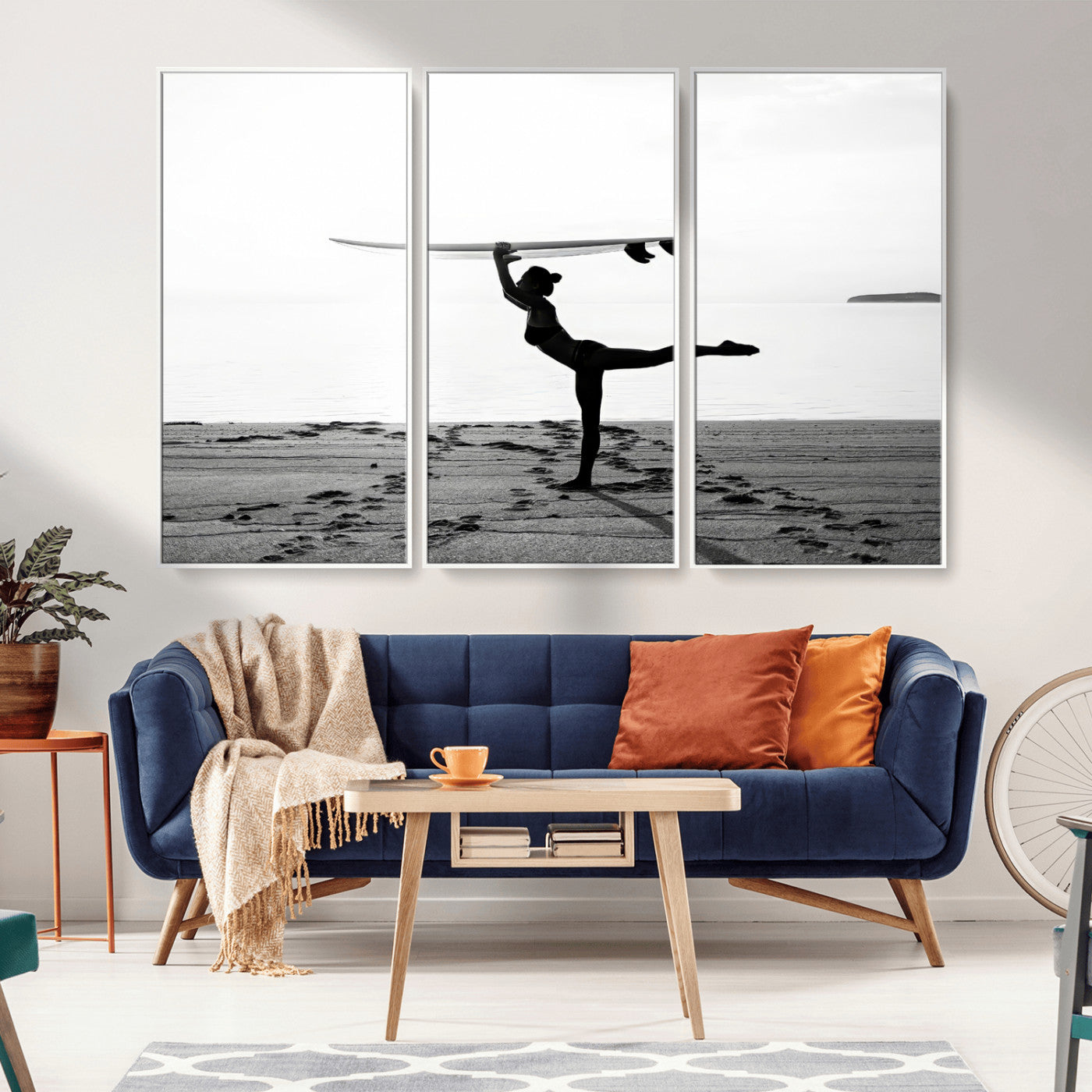 A woman balances a surfboard on her head while striking a yoga pose on the beach, silhouetted against a calm ocean horizon.