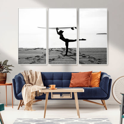 A woman balances a surfboard on her head while striking a yoga pose on the beach, silhouetted against a calm ocean horizon.